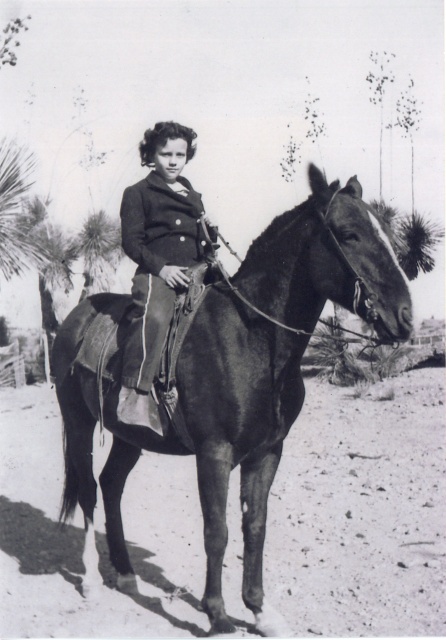 A black-and-white
photograph of a young girl, perhaps eight years old, astride a pony.
Her dark curly hair is cut short.  She is wearing a dark
double-breasted wool jacket and loose trousers, andfaces the camera
confidently.